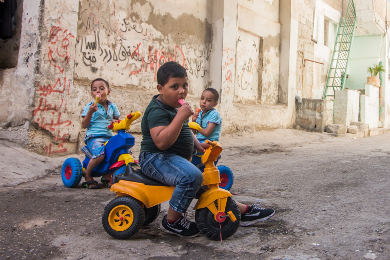 Malí motorkáři prohánějí své stroje úzkými uličkami uprchlického tábora